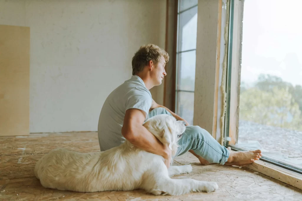 Pets - Do you Love or Hate Them? 5 Basic HOA Pet Rules 1 picture of a man with blonde hair looking out of a windom, with his arm around a fluffy white golden retriever