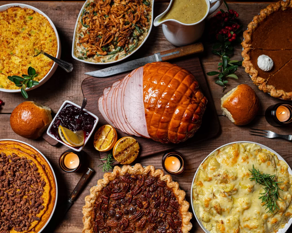 5 Ways to Celebrate Thanksgiving in Your Community 1 image of different thanksgiving dishes: ham, 4 pies, pumpkin and other food