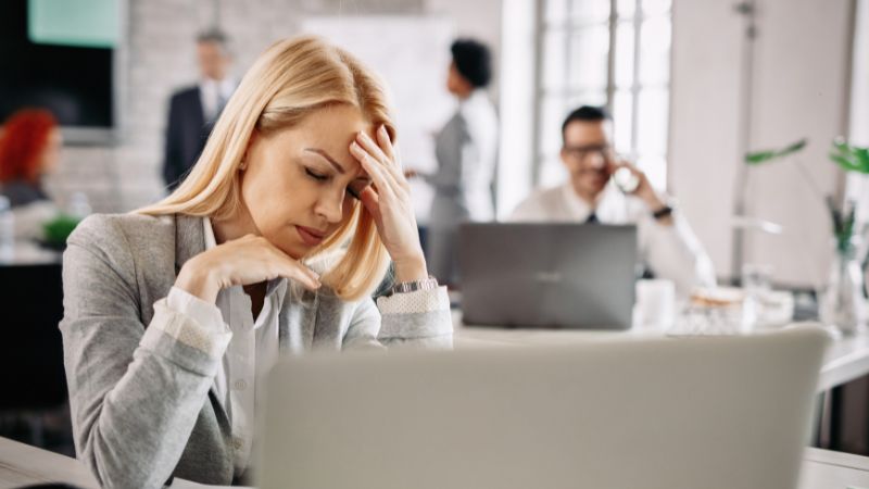 Unmasking Unethical HOA Board Members: Your Guide to Taking Action 1 The image shows a woman in an office, with her hand in her forehead and a stressed look on her face due to Unethical HOA Board Members.